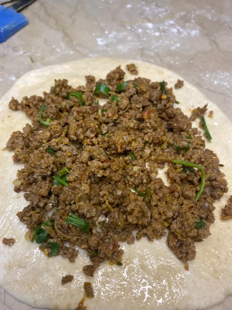Time to baste the rolled dough with egg; you can use an oil brush for this purpose. Also, spread the cooking oil on the surface of the rolled dough to add extra flavor and tenderness. Add the keema fillings, and close the dough by pinching all the sides individually. 